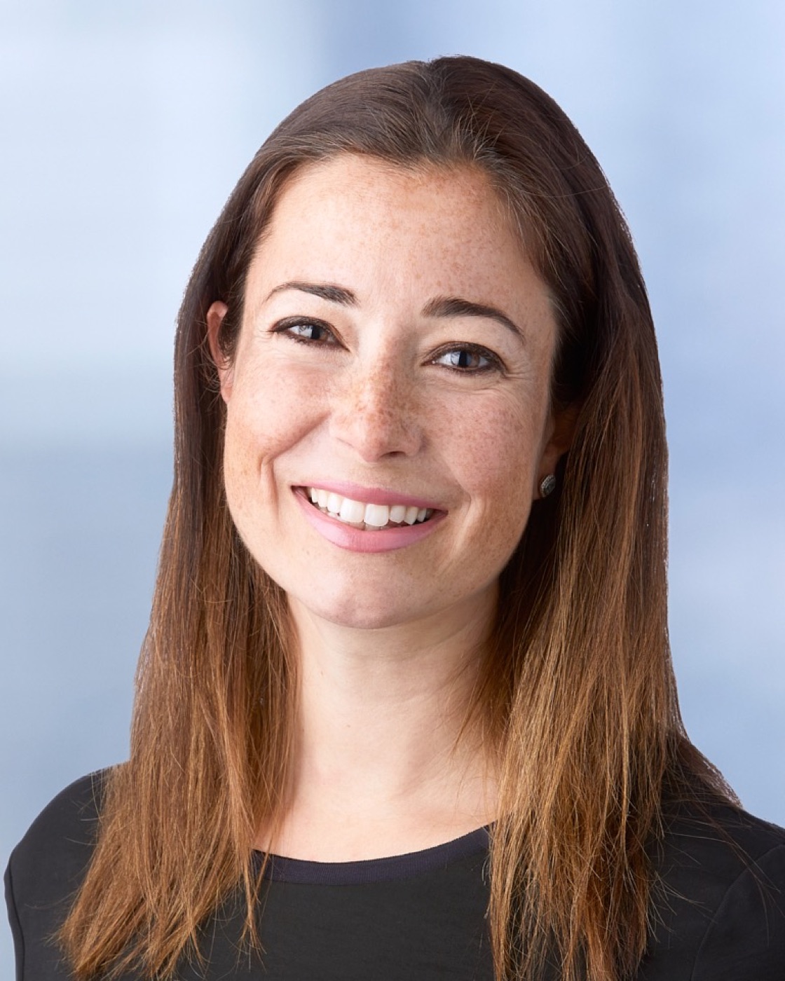 Corporate headshot of a woman in a dark top, soft blue background