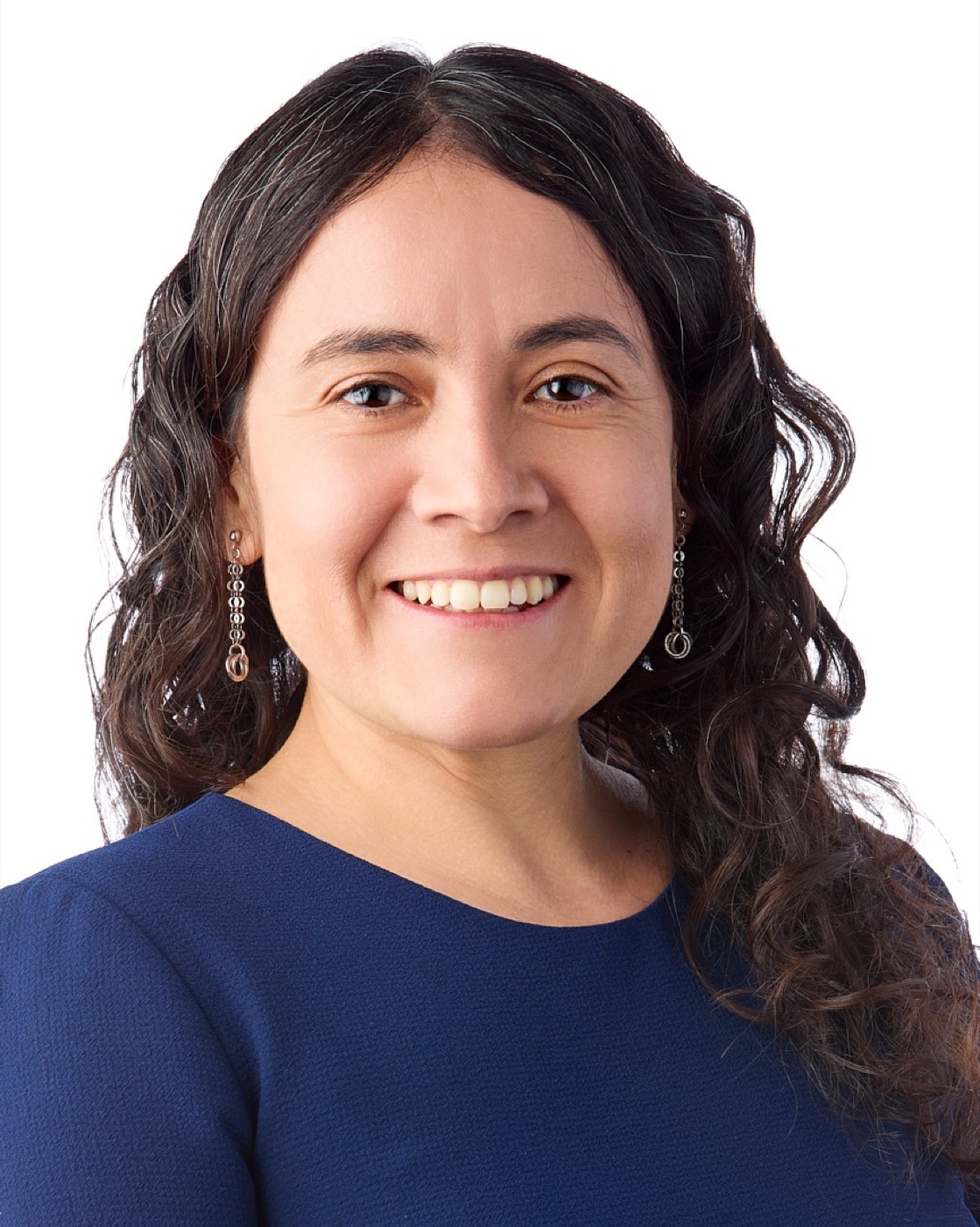 Corporate headshot of a woman with dark curls and a bright smile, navy top on white