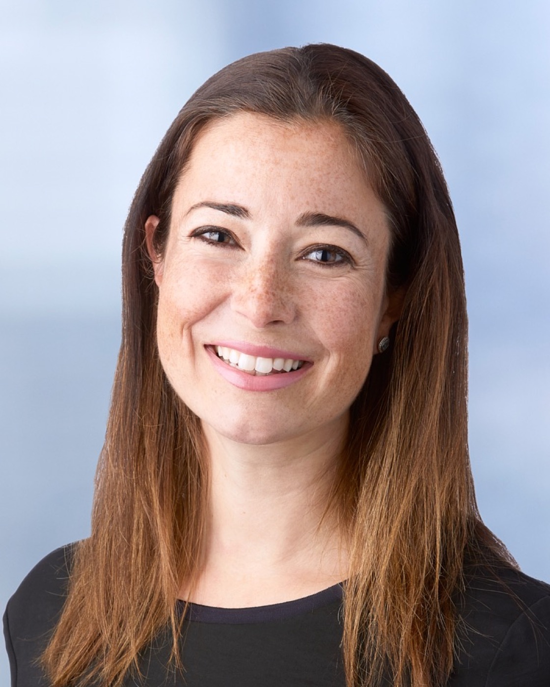 Corporate headshot of a woman in a dark top, soft blue background