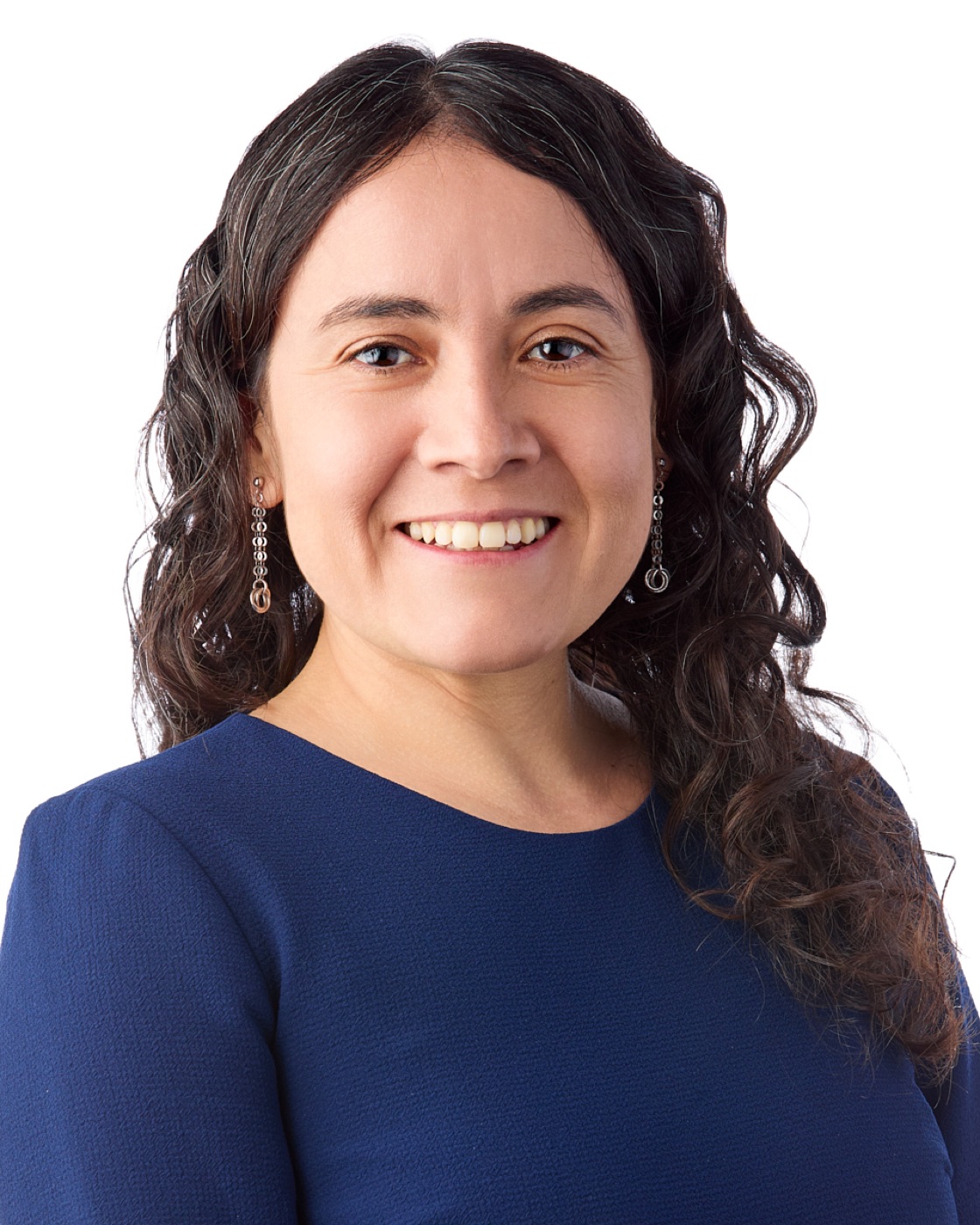 Corporate headshot of a woman with dark curls and a bright smile, navy top on white