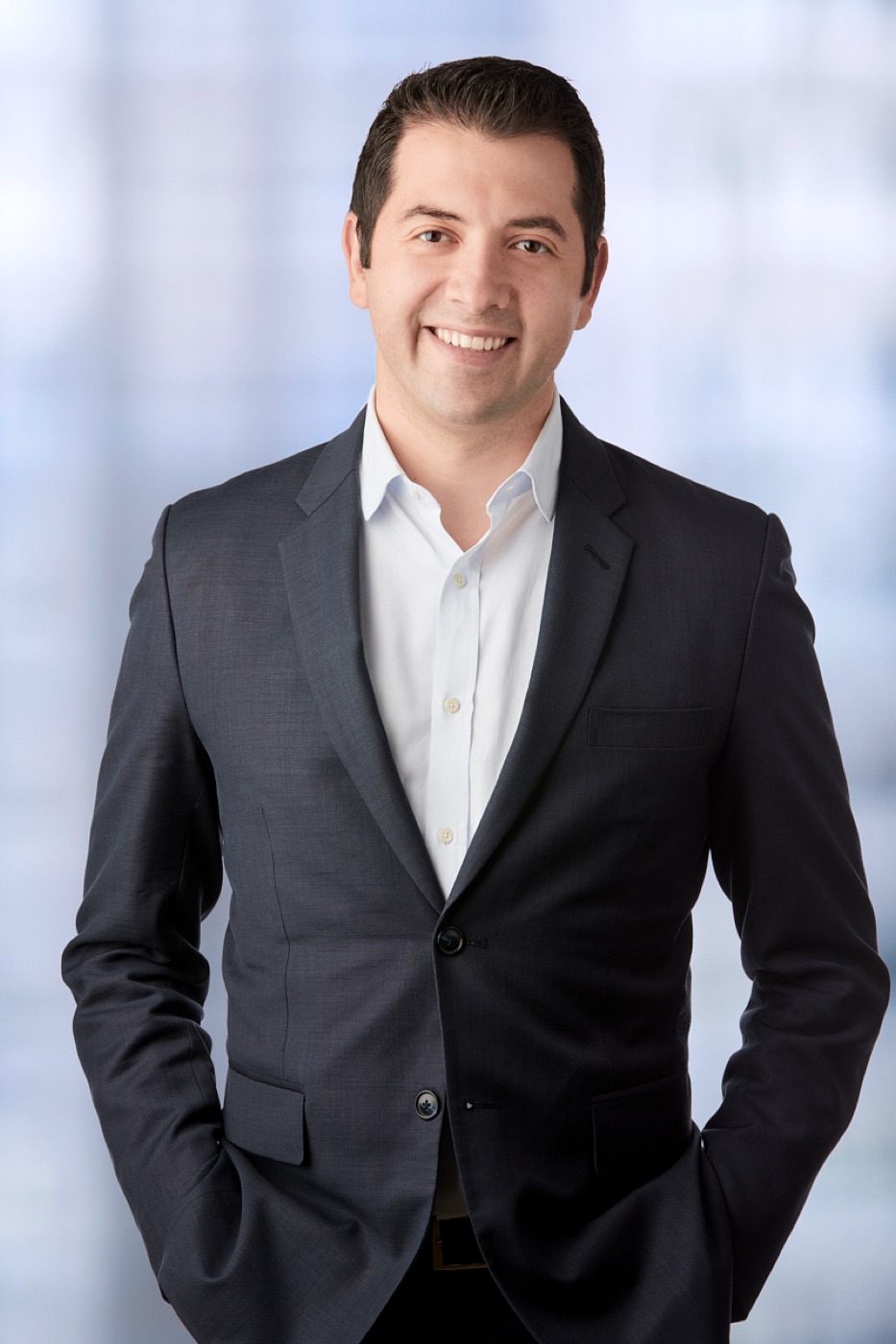 Studio corporate portrait of a man in a charcoal suit, hands in pockets
