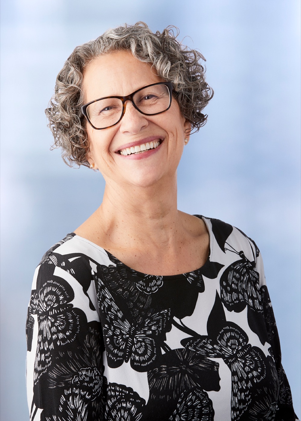 Studio portrait of a woman with gray curls and glasses caught mid-laugh