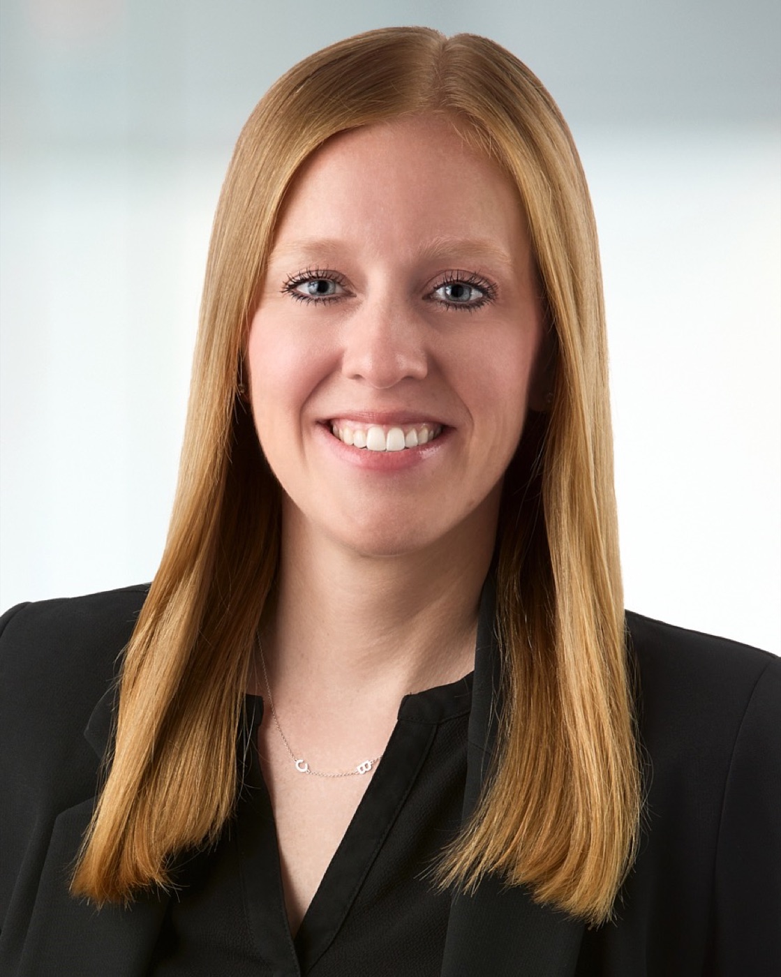 Corporate headshot of a woman in a black blazer, bright office background