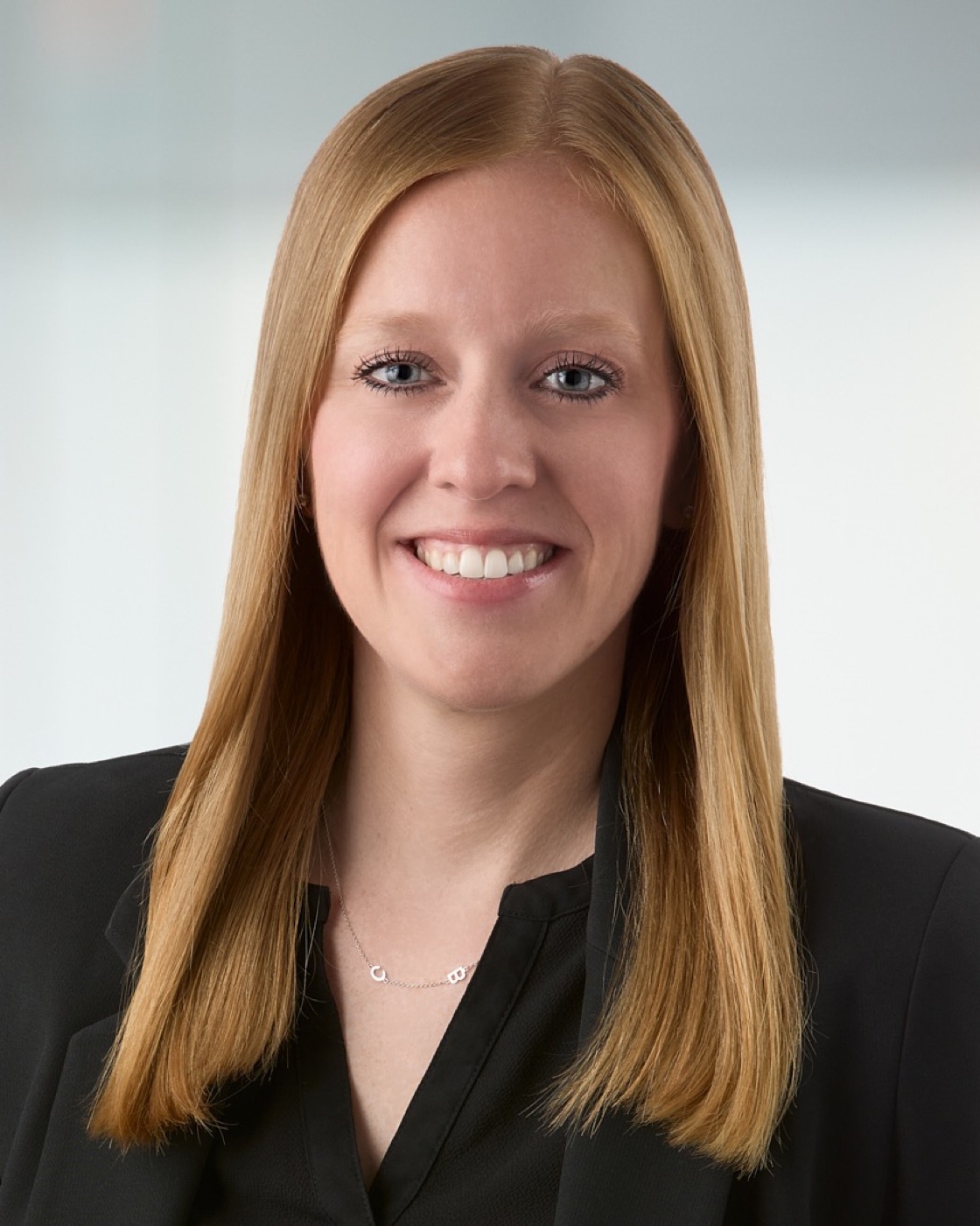 Corporate headshot of a woman in a black blazer, bright office background